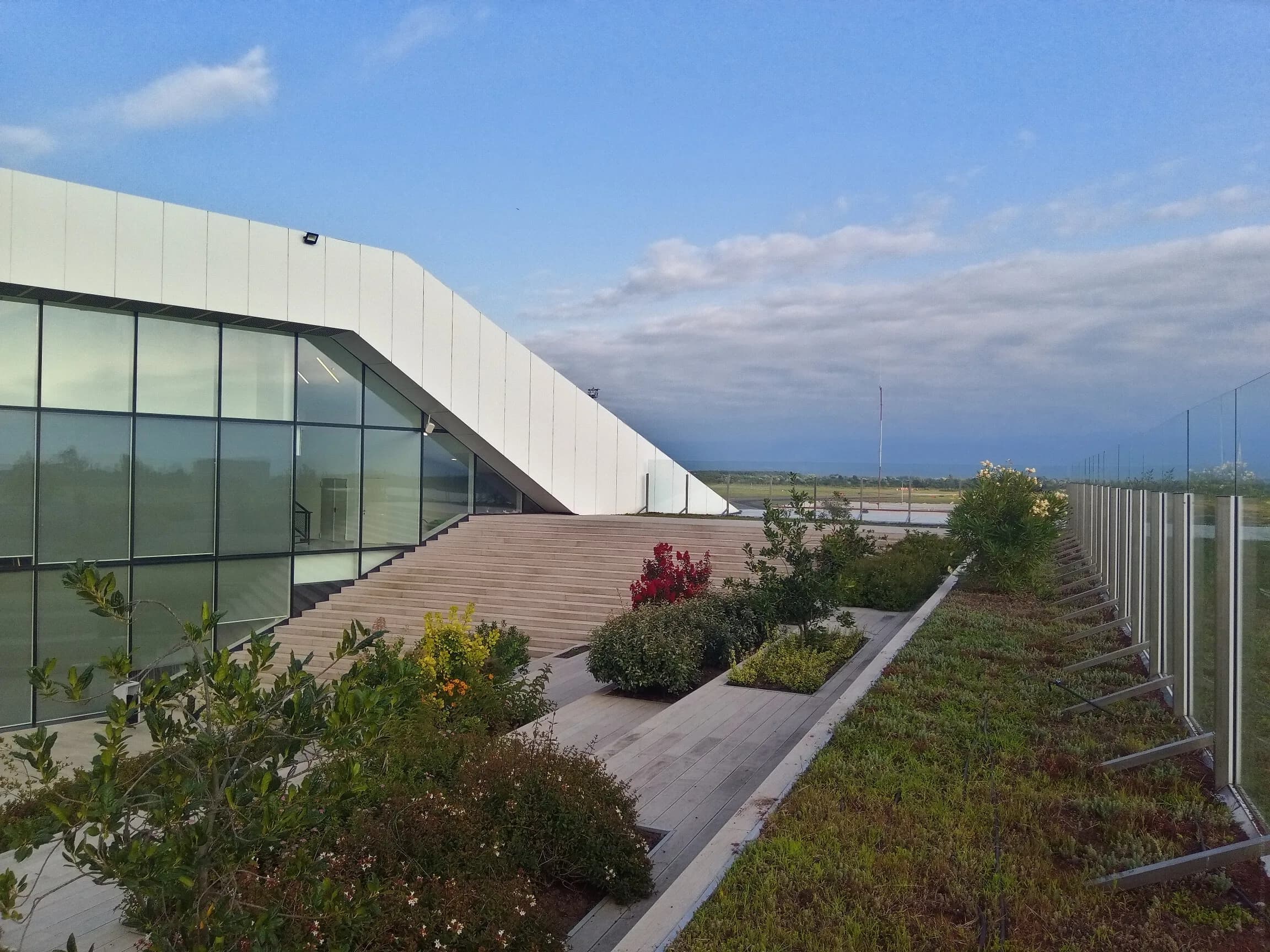 The white sloping facade and planted roof terrace of Kutaisi International Airport's terminal, with the airfield beyond