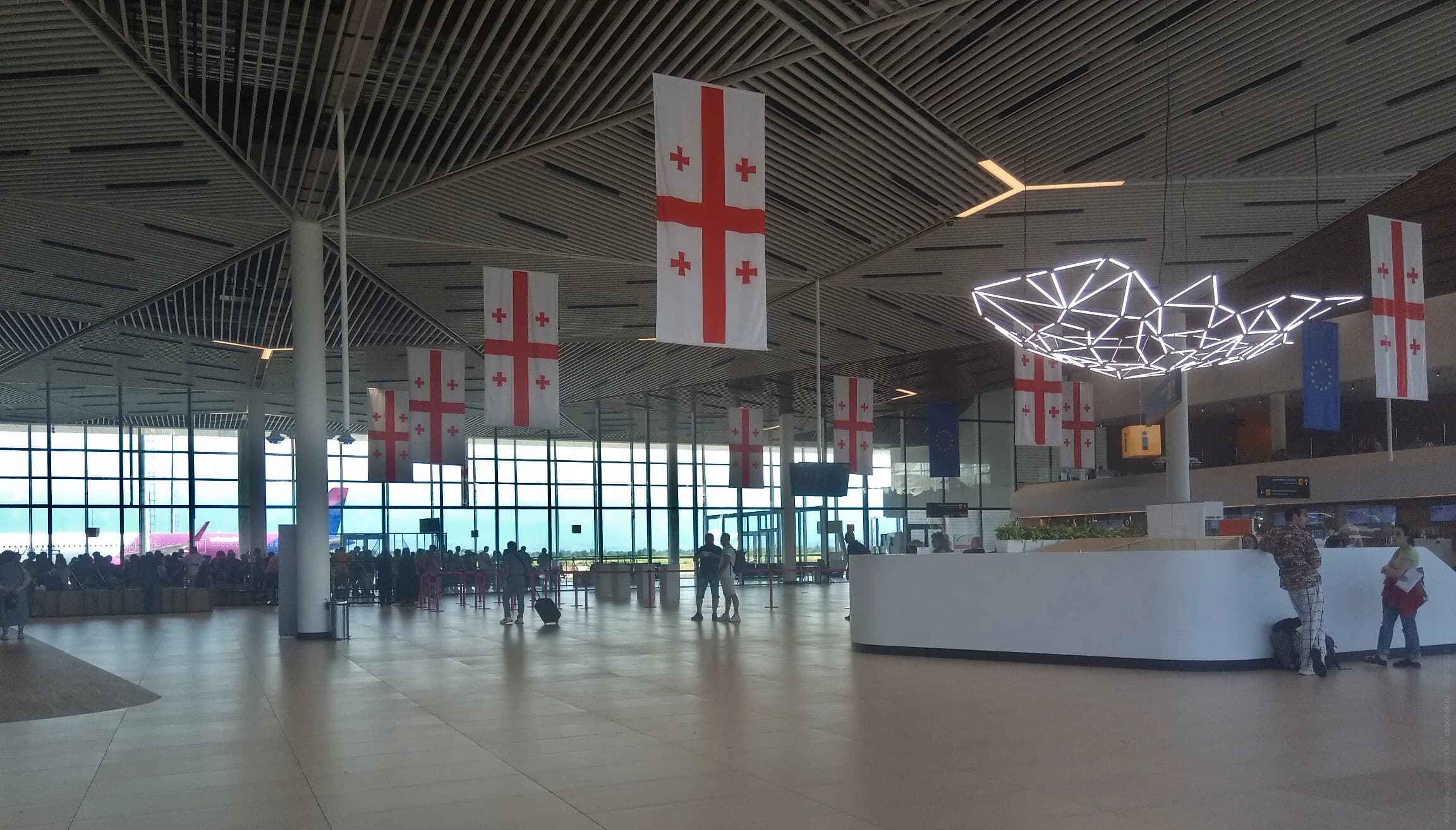 The check-in hall inside Kutaisi International Airport, Georgian flags overhead and a Wizz Air aircraft through the glass