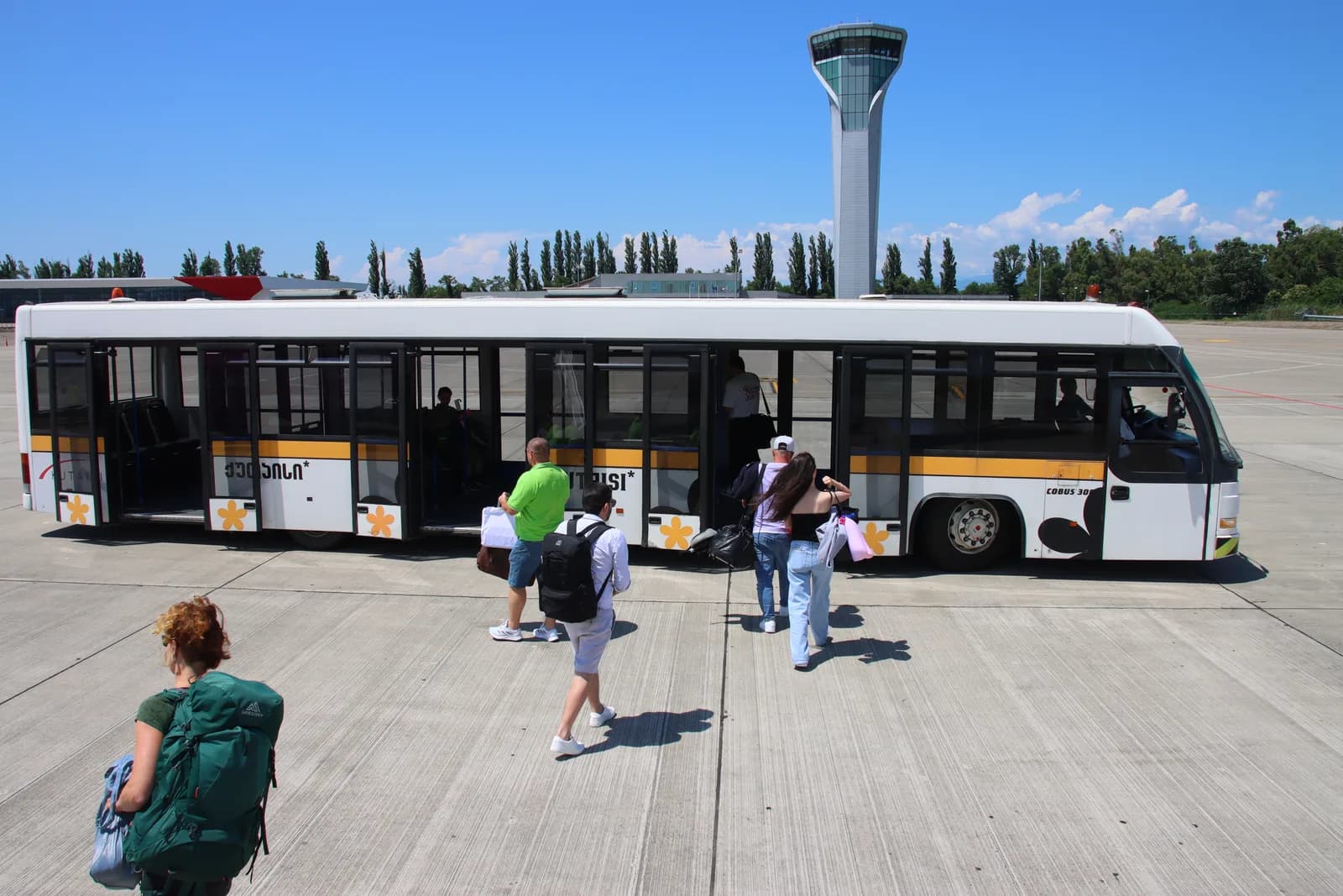 Passengers boarding the apron shuttle bus at Kutaisi International Airport, with the control tower rising behind