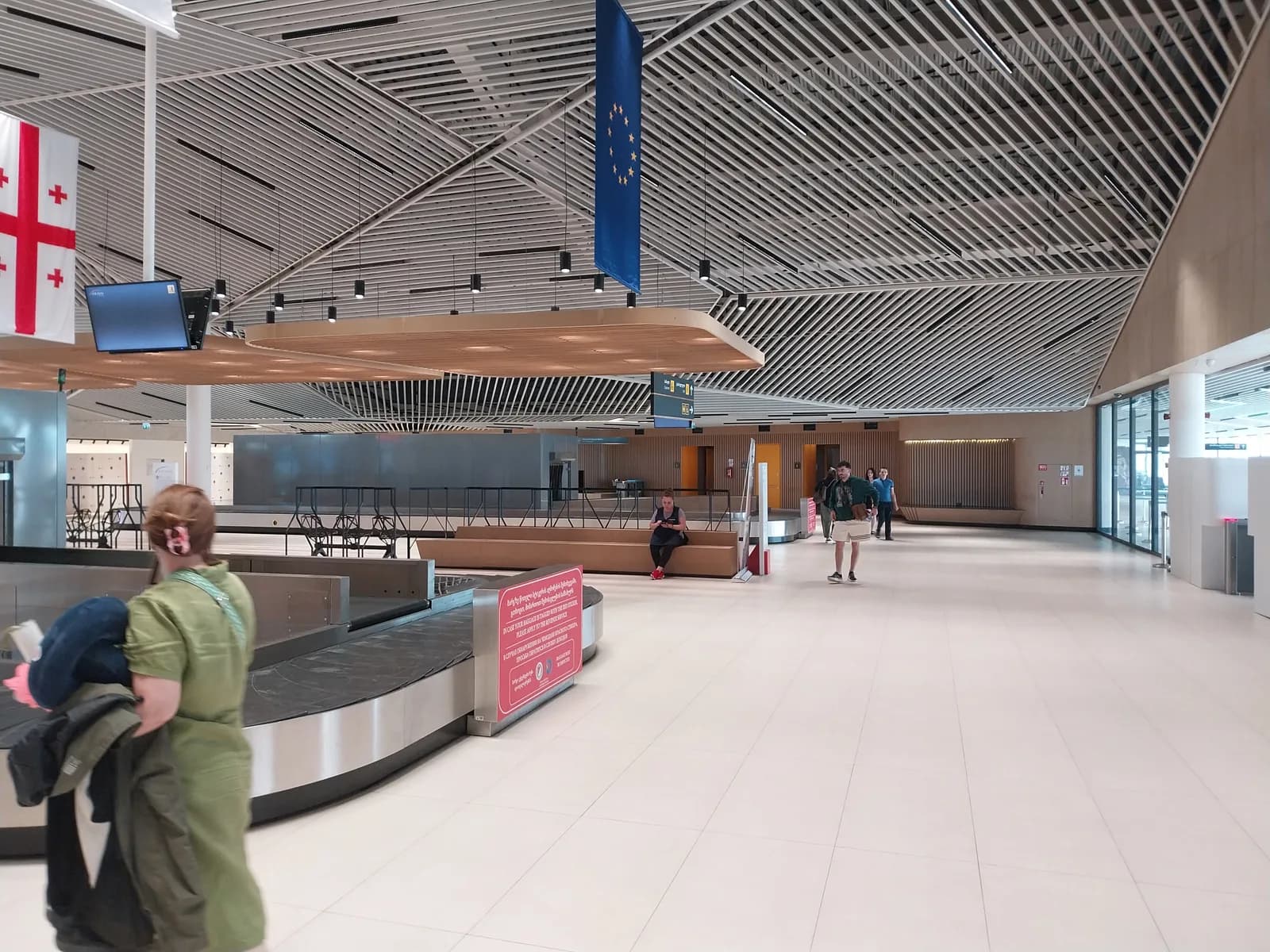 The baggage reclaim hall at Kutaisi International Airport, a single carousel under the timber-slatted ceiling with Georgian and EU flags above