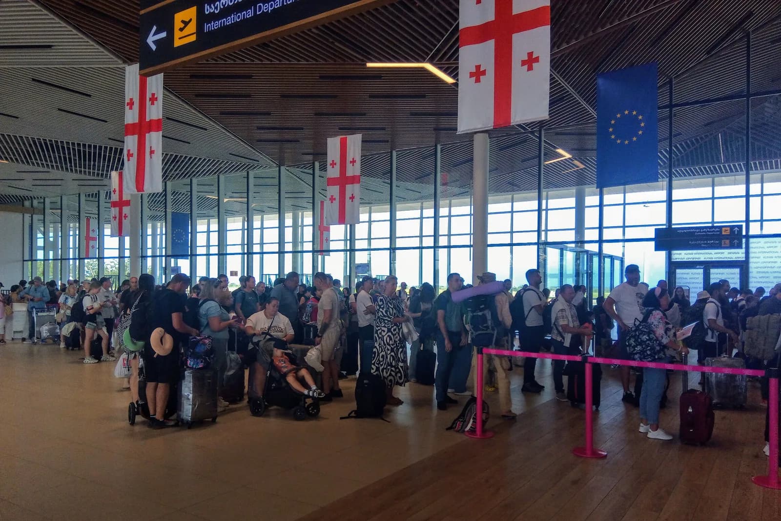 Passengers queueing for international departures at Kutaisi International Airport, Georgian and EU flags hanging from the timber-slatted ceiling